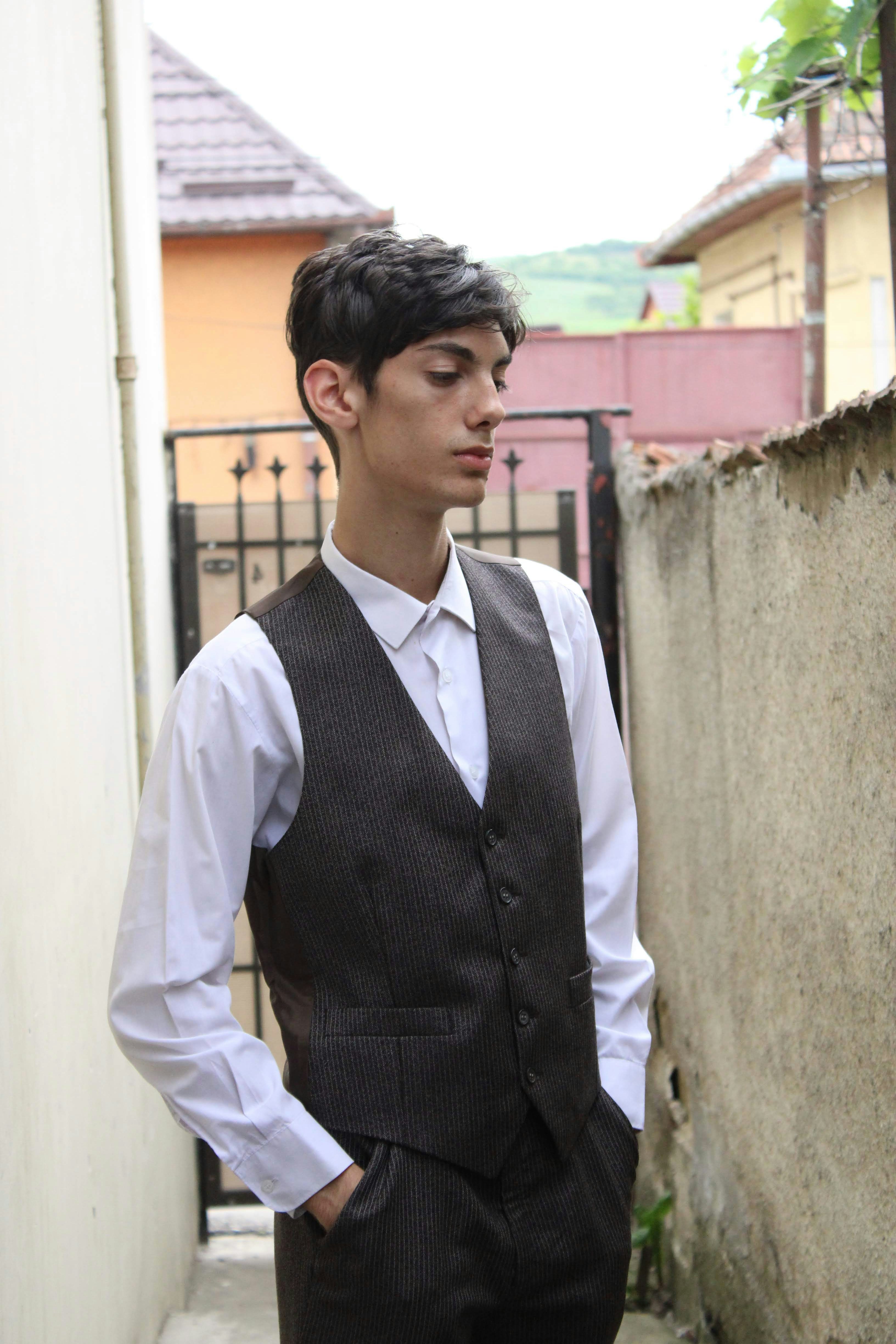 a man in a vest and tie standing next to a wall