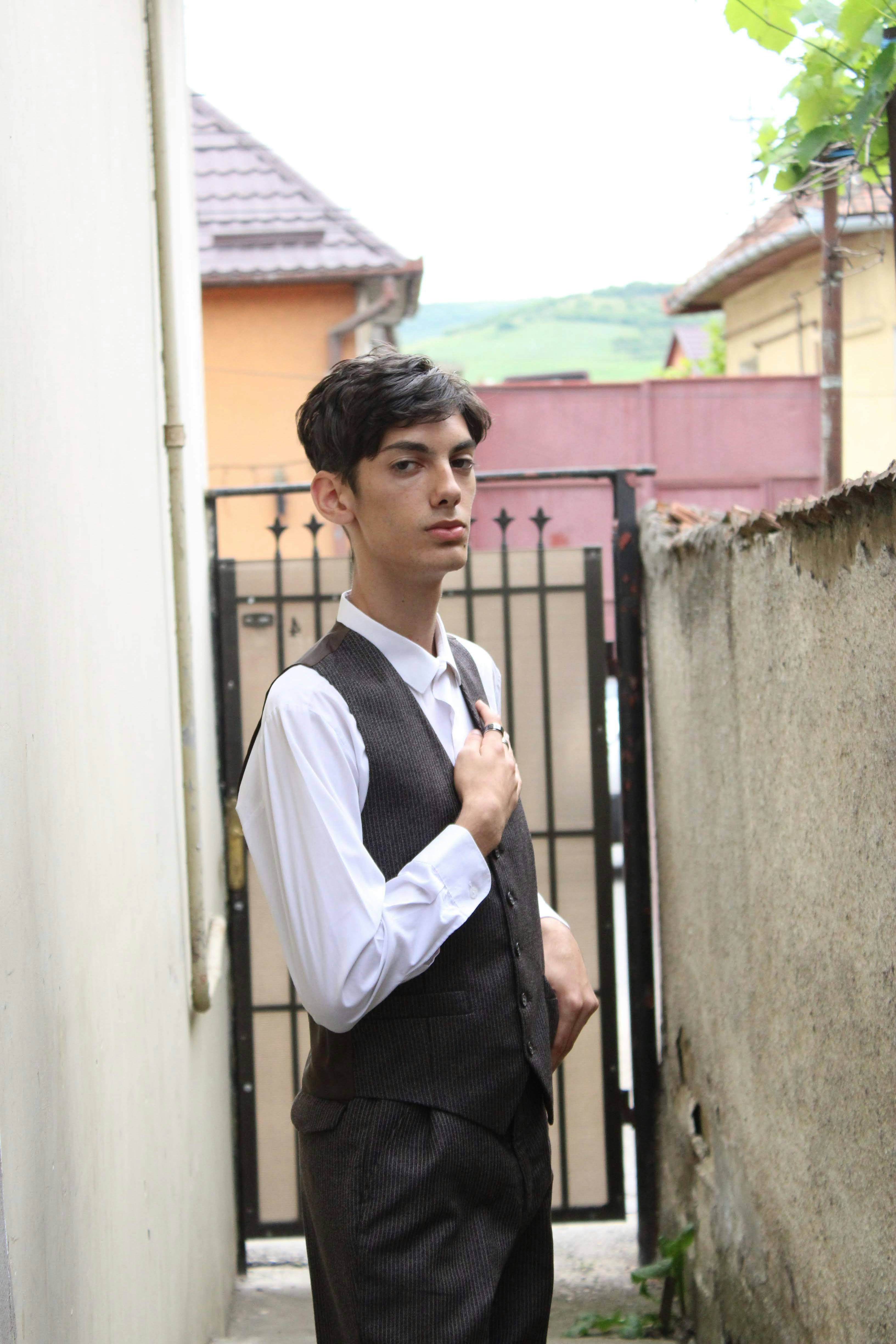 a man in a vest and tie standing in front of a gate
