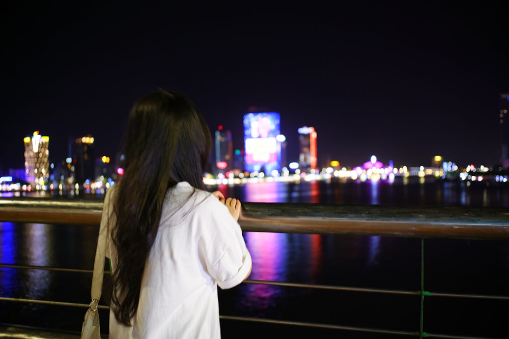 a woman standing on a bridge looking at the city lights