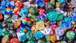 A vibrant assortment of multicolored polyhedral dice featuring various numeric values and designs. The dice in the collection display a wide range of colors, patterns, and materials including solid, translucent, glittery, and marbled effects.