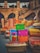 A vibrant display of colorful cushions and textiles is set against a rustic stone backdrop. The bright fabrics feature intricate patterns and bold colors, suggesting a lively market or artisan shop. The stone structure has arches and an outdoor staircase, adding to the traditional and historic ambiance.
