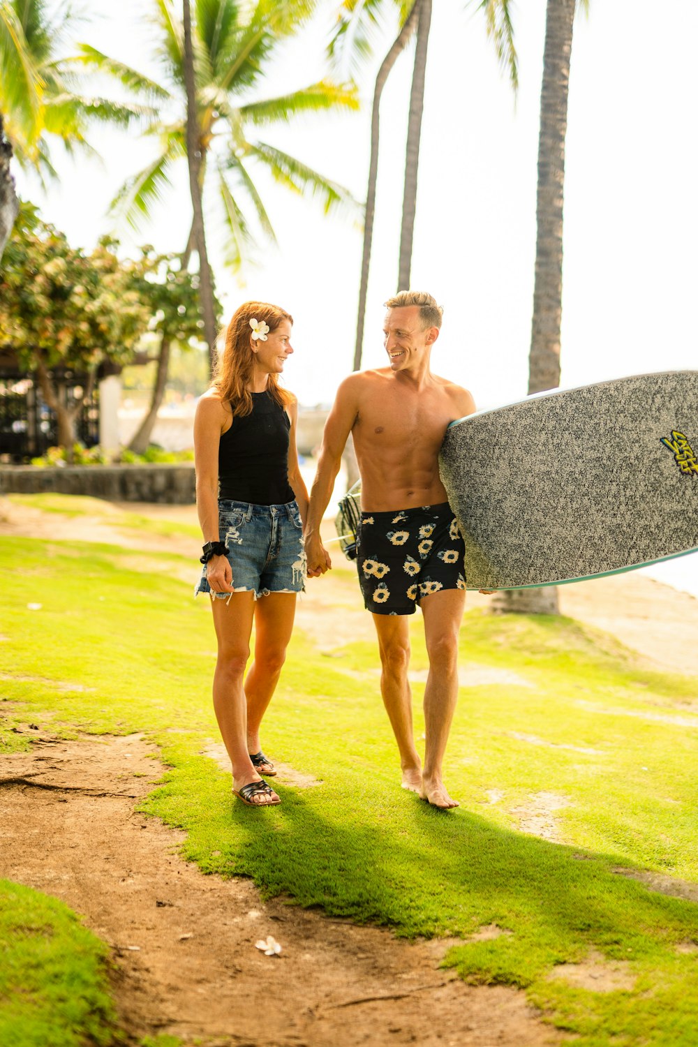 a man and a woman walking down a path holding a surfboard