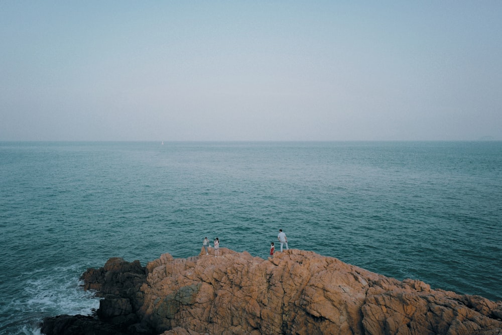a couple of people standing on top of a rock near the ocean