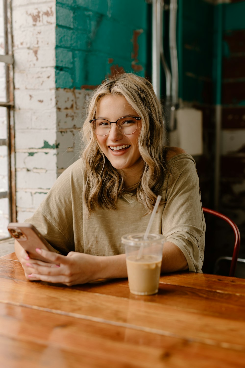 a woman sitting at a table with a drink and cell phone