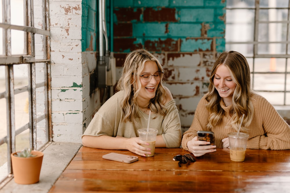 two women sitting at a table looking at a cell phone