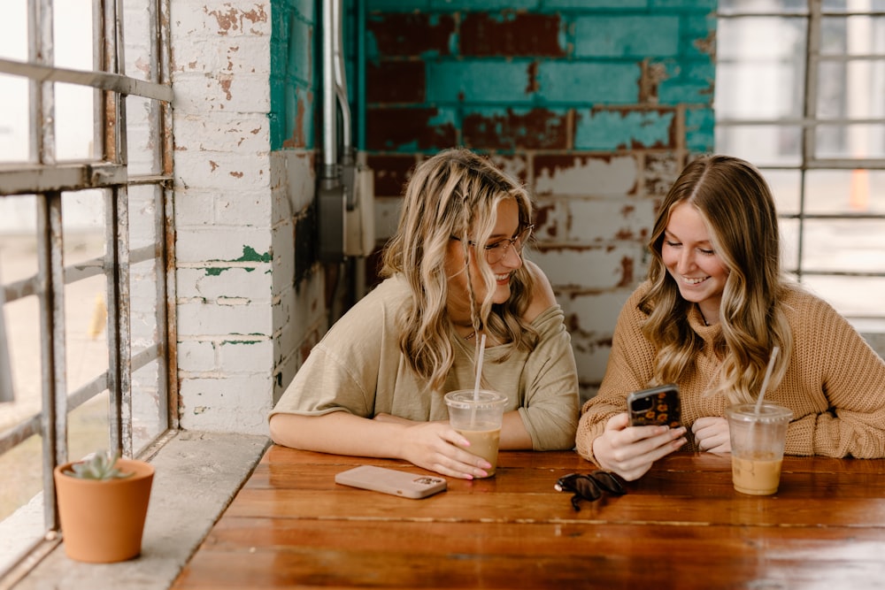 two women sitting at a table looking at a cell phone