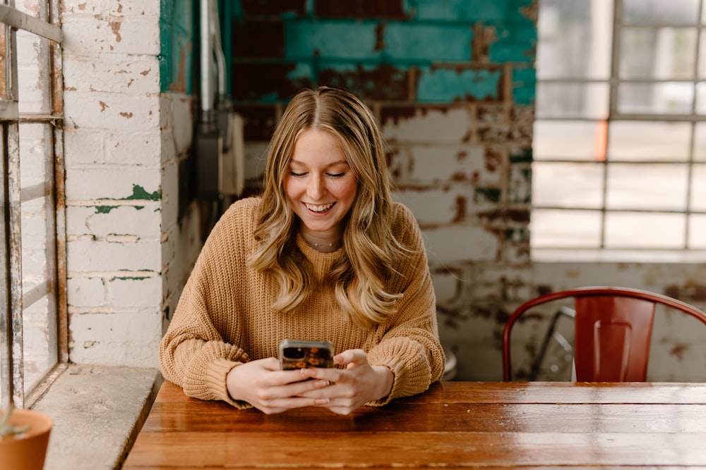 uma mulher sentada em uma mesa olhando para seu telefone celular