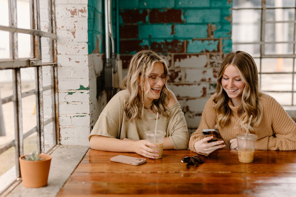 deux femmes assises à une table regardant un téléphone portable