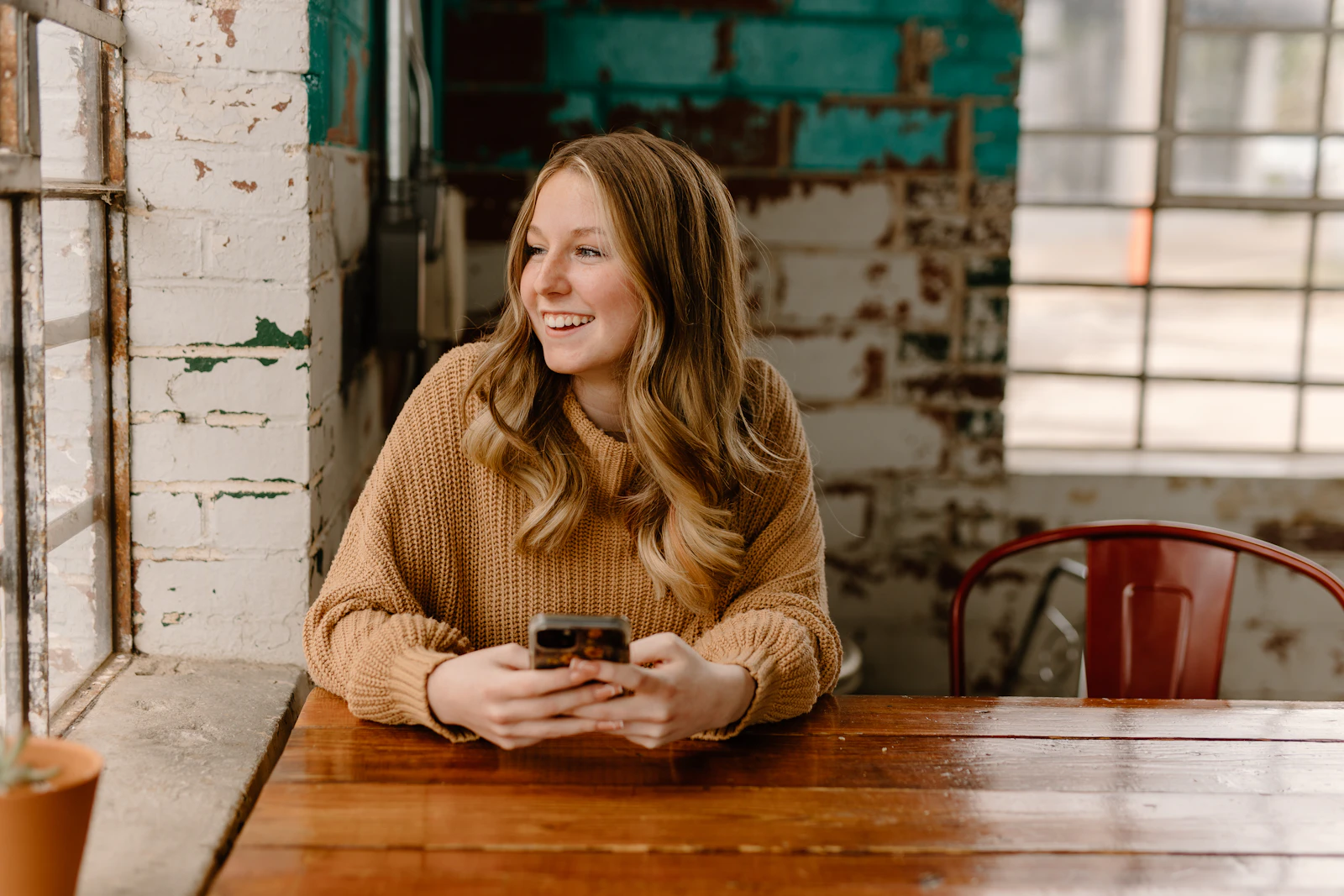 A smiling woman holding her phone at a wooden cafe table