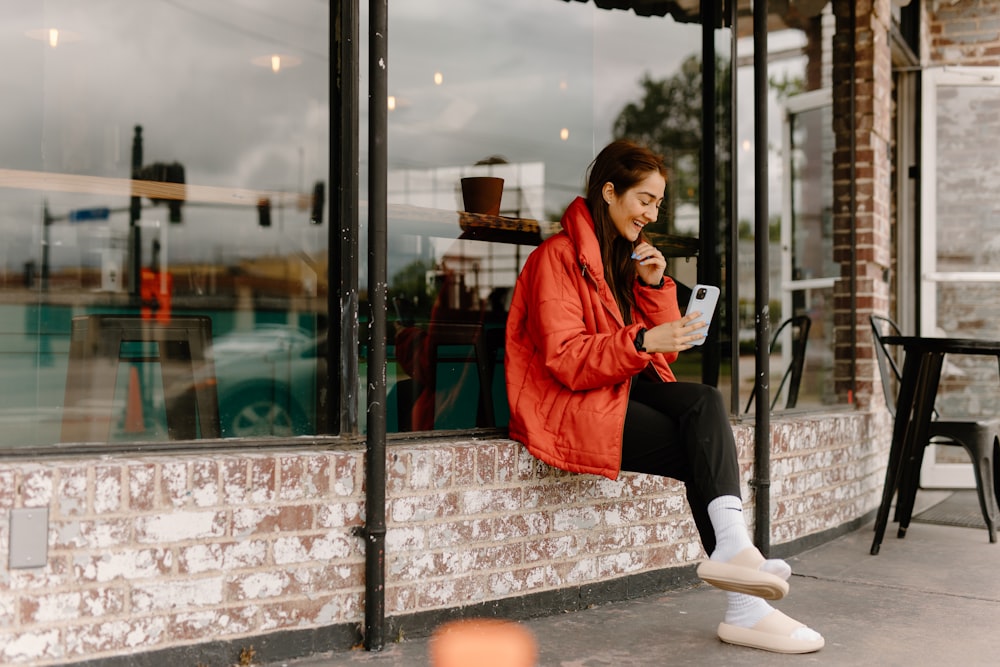 a woman sitting on a window sill looking at her cell phone