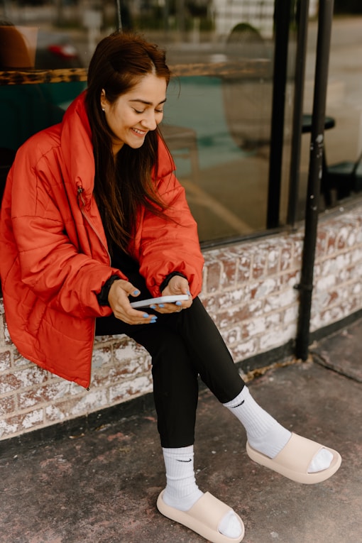 a woman sitting on a window sill looking at her cell phone