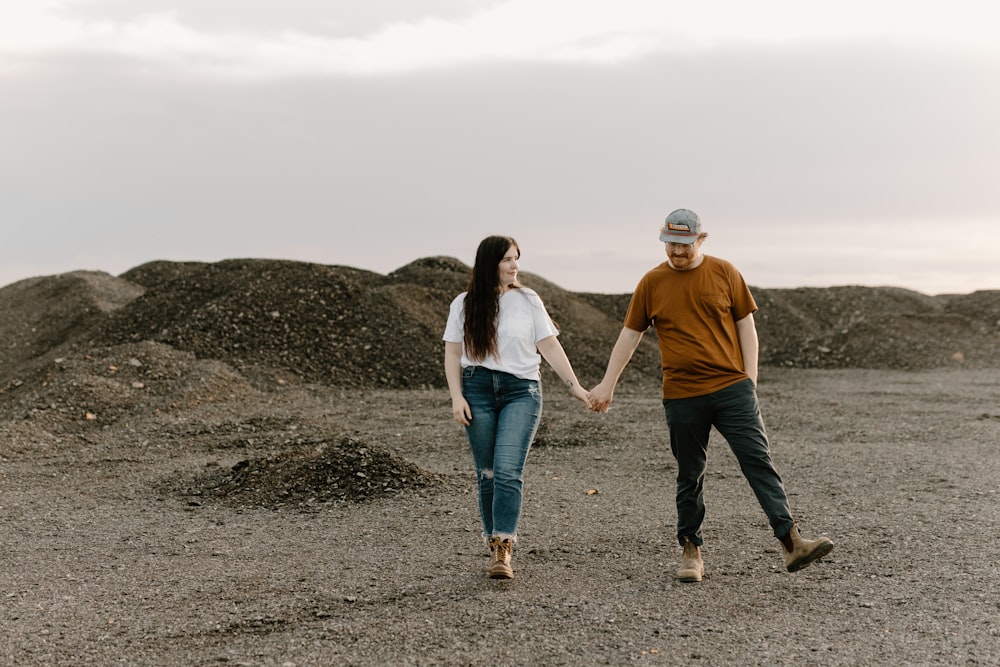 a man and a woman holding hands while walking through a field