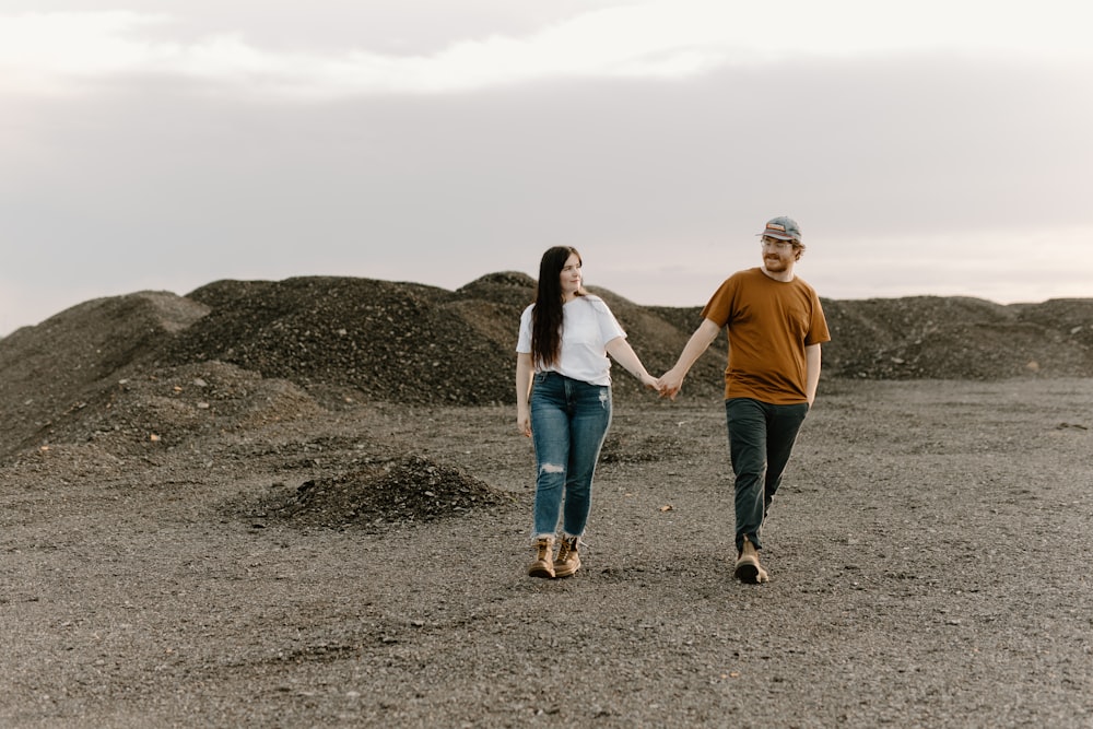 a man and a woman holding hands while walking through a dirt field