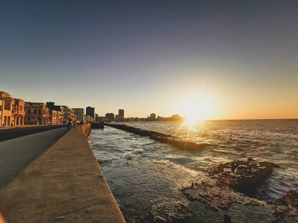 the sun is setting over the water near a city