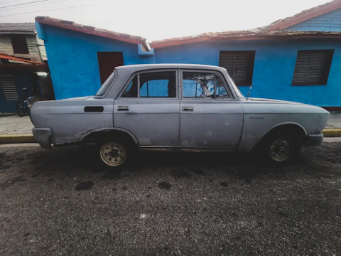 an old car parked in front of a blue building