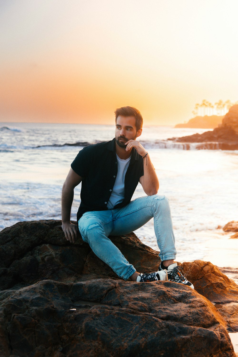 a man sitting on top of a rock near the ocean
