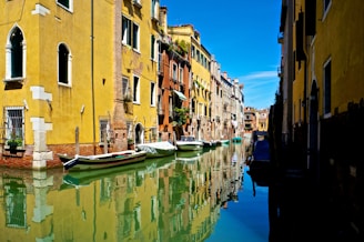 a row of boats floating on top of a river next to tall buildings