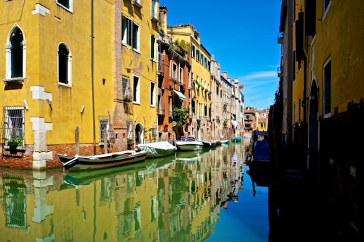 a row of boats floating on top of a river next to tall buildings