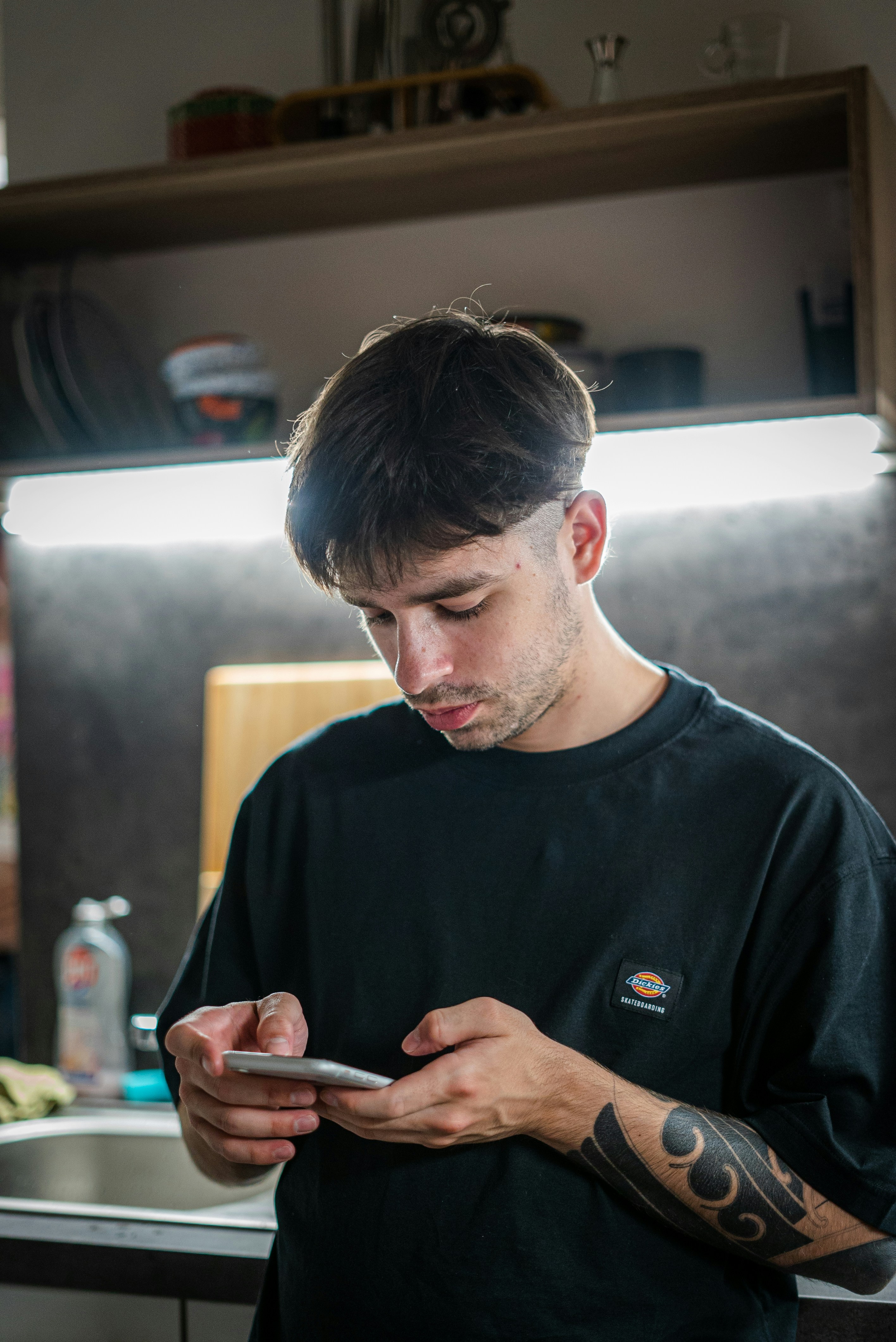 Un uomo in piedi in una cucina che guarda il suo cellulare