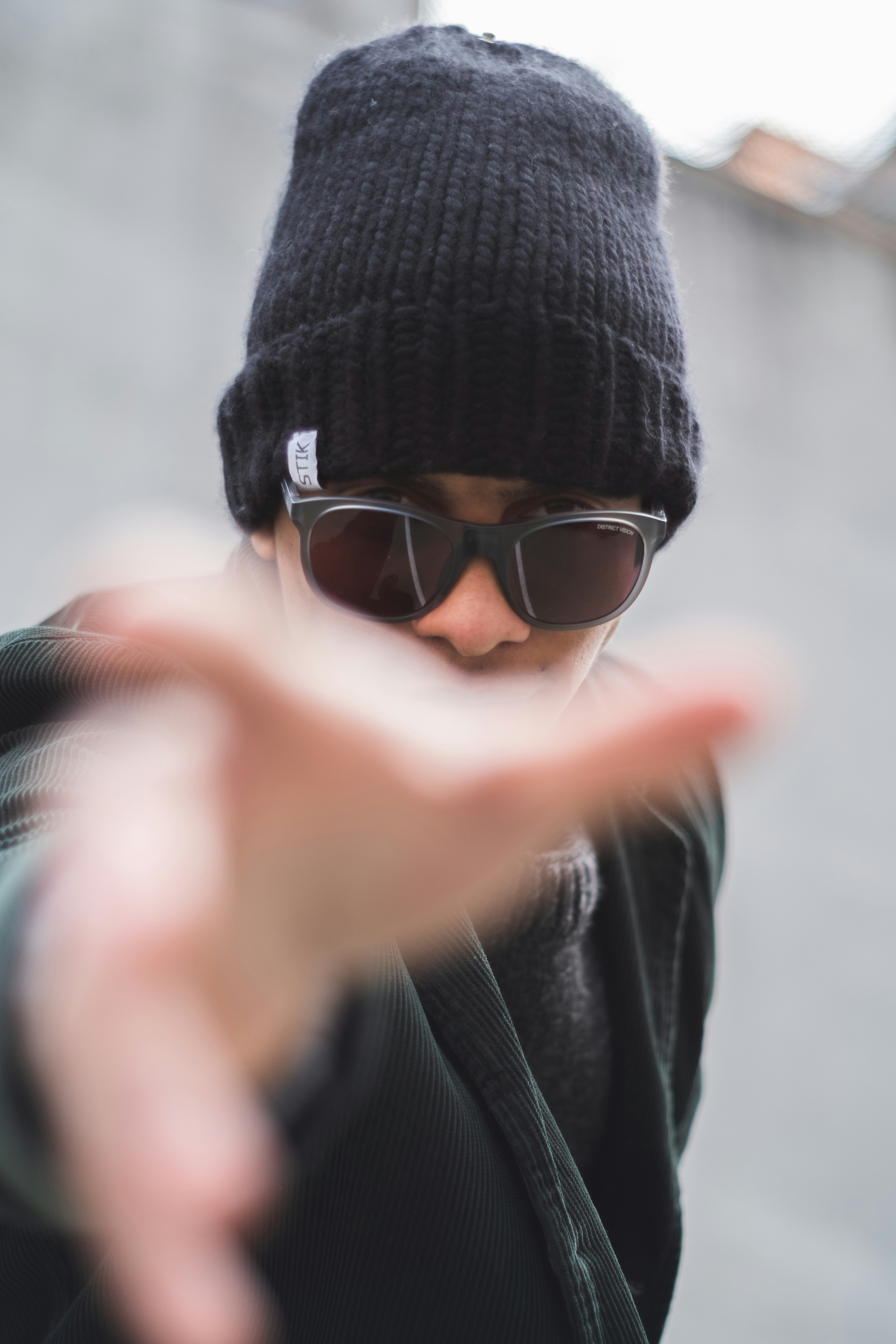 a man wearing sunglasses and a beanie making a hand gesture