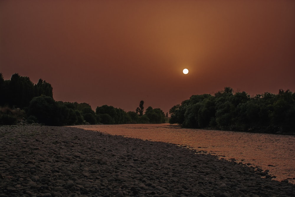 the sun is setting over a river and trees