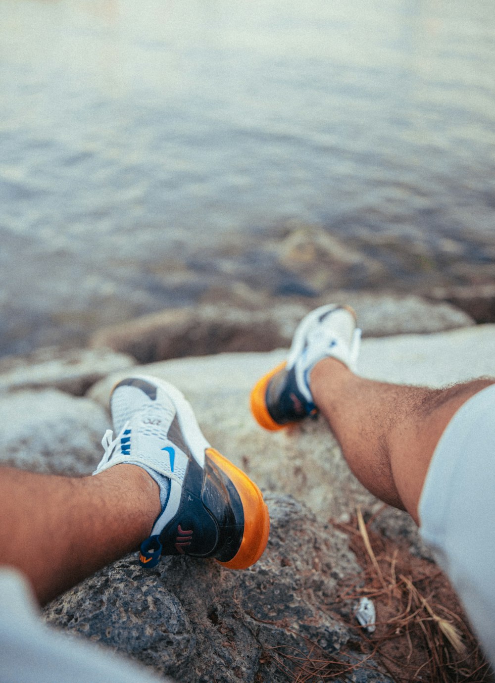 a pair of feet resting on a rock next to a body of water