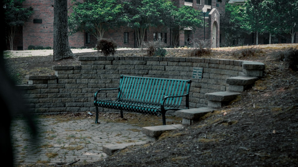 a green bench sitting next to a stone wall