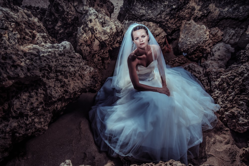 a woman in a wedding dress sitting on rocks