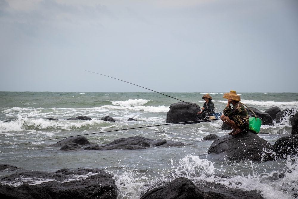 two men fishing on rocks in the ocean