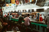 Happy young people sharing tacos and drinks around a bright red and yellow fast-food counter.