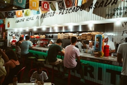 Happy young people sharing tacos and drinks around a bright red and yellow fast-food counter.
