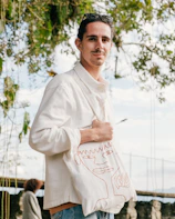 Mood shot of someone wearing a black Kratz Korner tee and holding a matching tote bag outdoors.