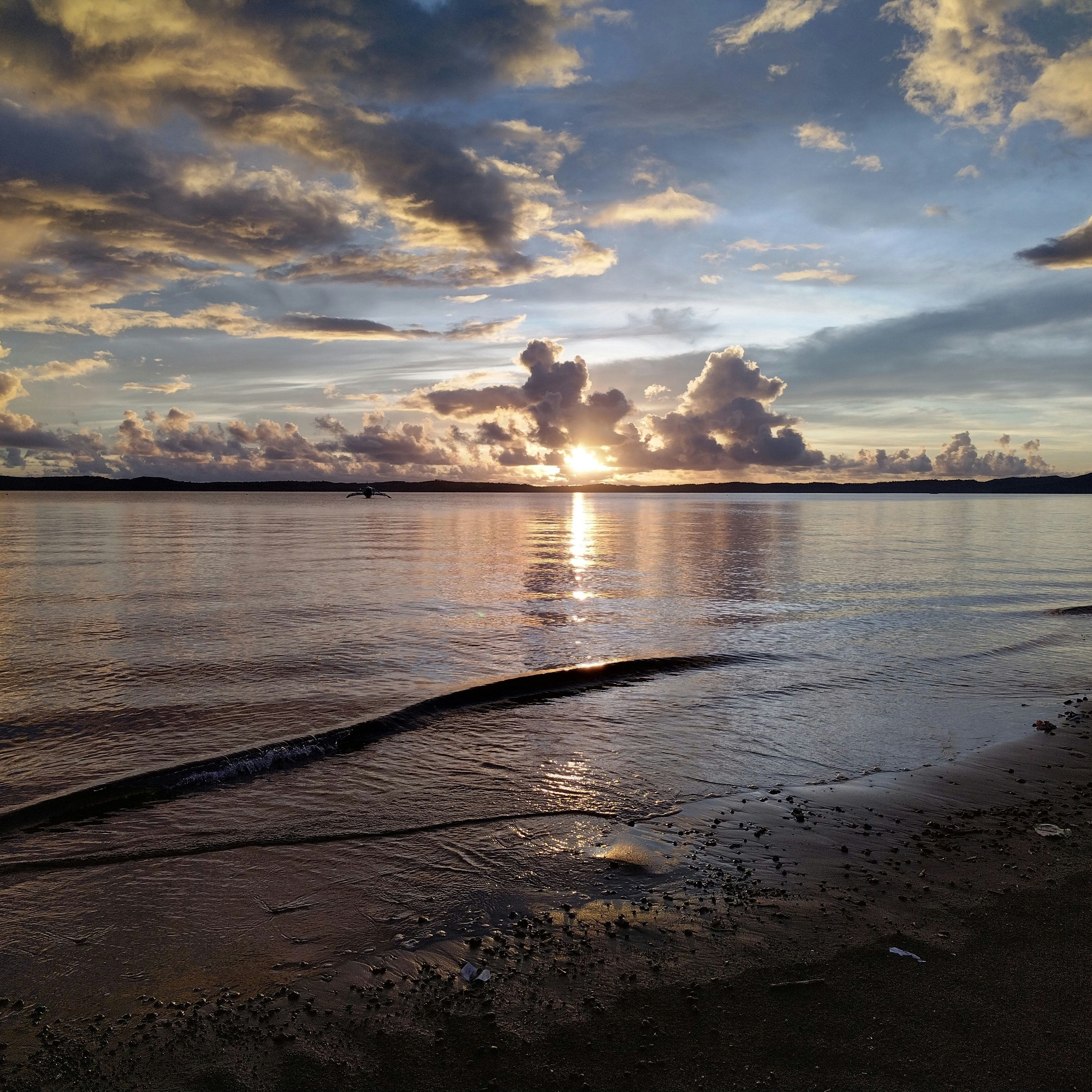 the sun is setting over the water on the beach