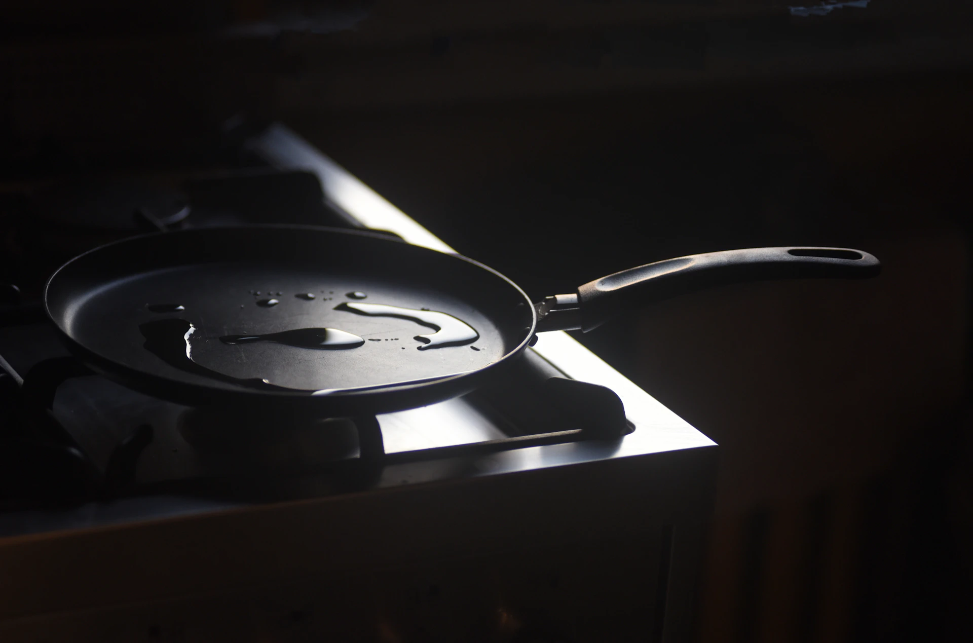 Black frying pan on a stove caught in a hard diagonal shaft of light