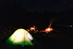 Camping gear set up around a glowing campfire at dusk