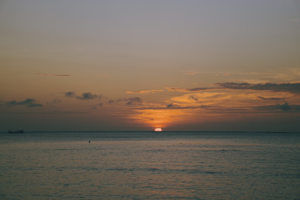 the sun is setting over the ocean with a boat in the distance