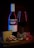 A bottle of Cabernet Merlot wine with a filled glass sits on a wooden surface. Nearby are a wedge of cheese, halved figs, and a bunch of grapes. Soft lighting highlights textures and colors, giving a sense of luxury and indulgence.