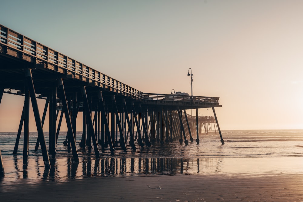 Un muelle en una playa con la puesta de sol de fondo