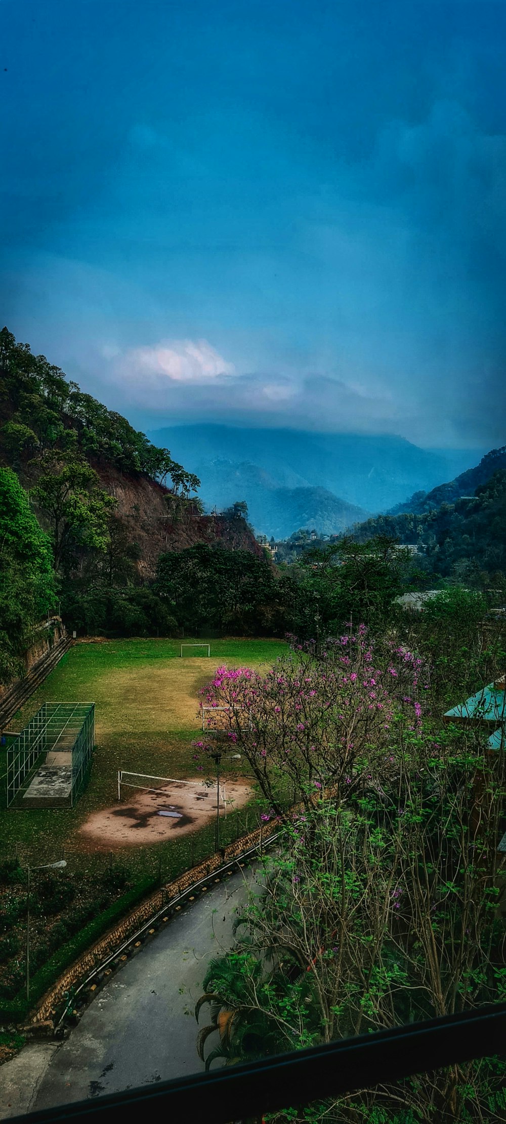 a grassy field with a tennis court and mountains in the background