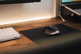 A sleek modern computer setup with a glowing keyboard and ergonomic mouse on a wooden desk.