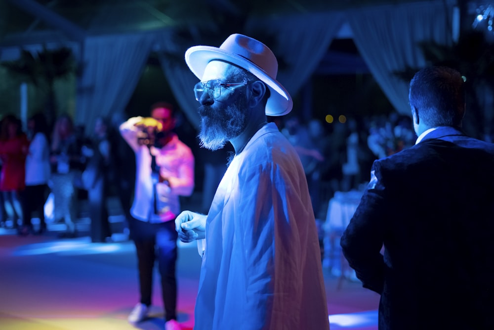 a man in a white hat and sunglasses standing in front of a group of people