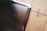 A close-up view of a scratched tablet or phone screen next to a wooden surface. The screen shows multiple scratches and the wooden surface has a natural grain pattern.
