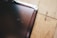 A close-up view of a scratched tablet or phone screen next to a wooden surface. The screen shows multiple scratches and the wooden surface has a natural grain pattern.