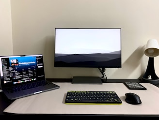 a desk with a laptop, keyboard, mouse and monitor