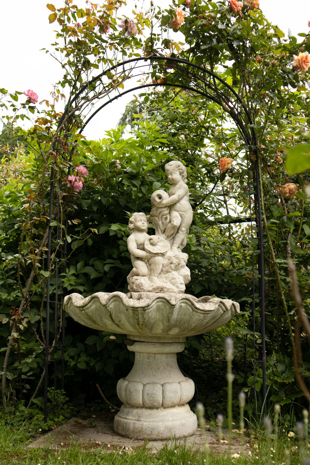 a stone fountain in a garden surrounded by flowers