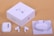 A set of white wireless earbuds is displayed alongside the packaging. The items include two individual earbuds, a compact charging case, a neatly coiled charging cable, and a white square packaging box labeled 'AirPods Pro'. The background is a neutral beige color.