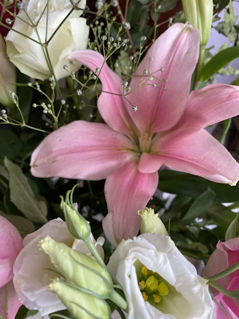A close-up of a beautifully arranged flower bouquet featuring roses, lilies, and greenery.