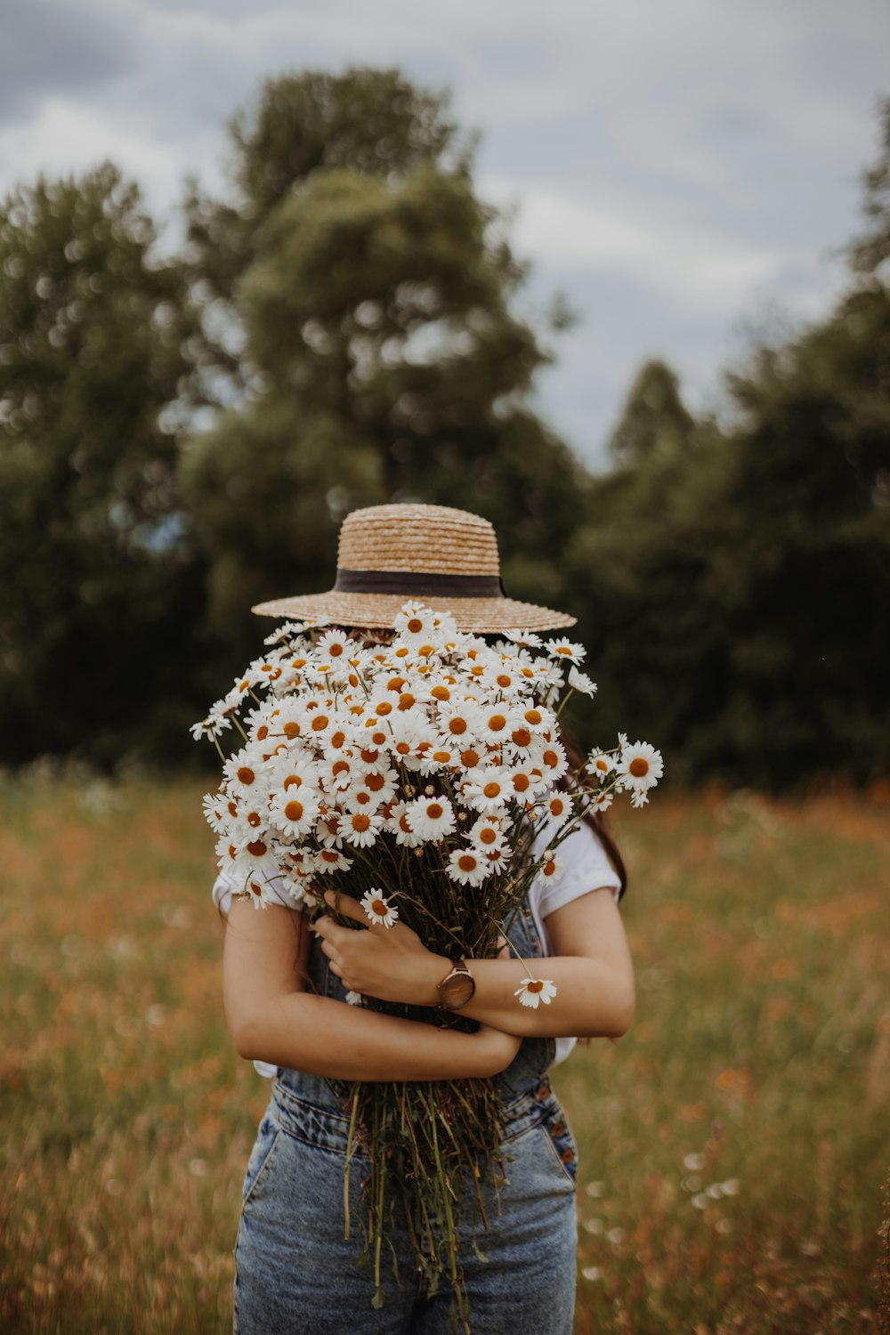 a woman holding a bunch of daisies in a field