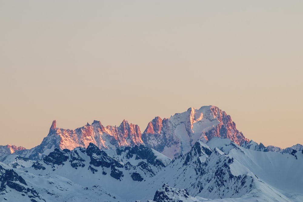 a mountain range covered in snow at sunset