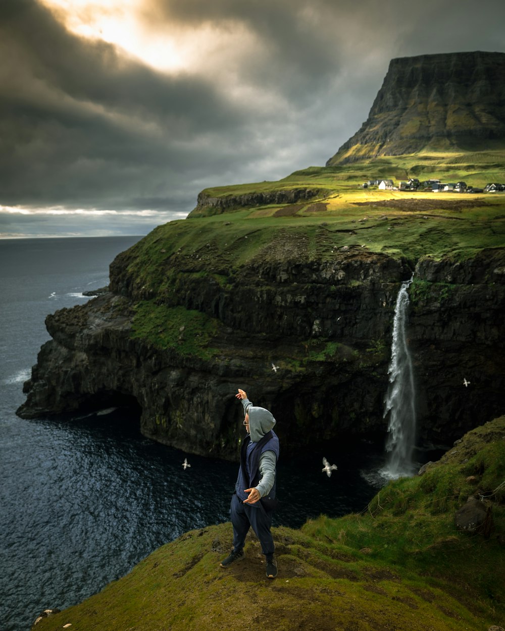 a man standing on top of a lush green hillside next to a waterfall